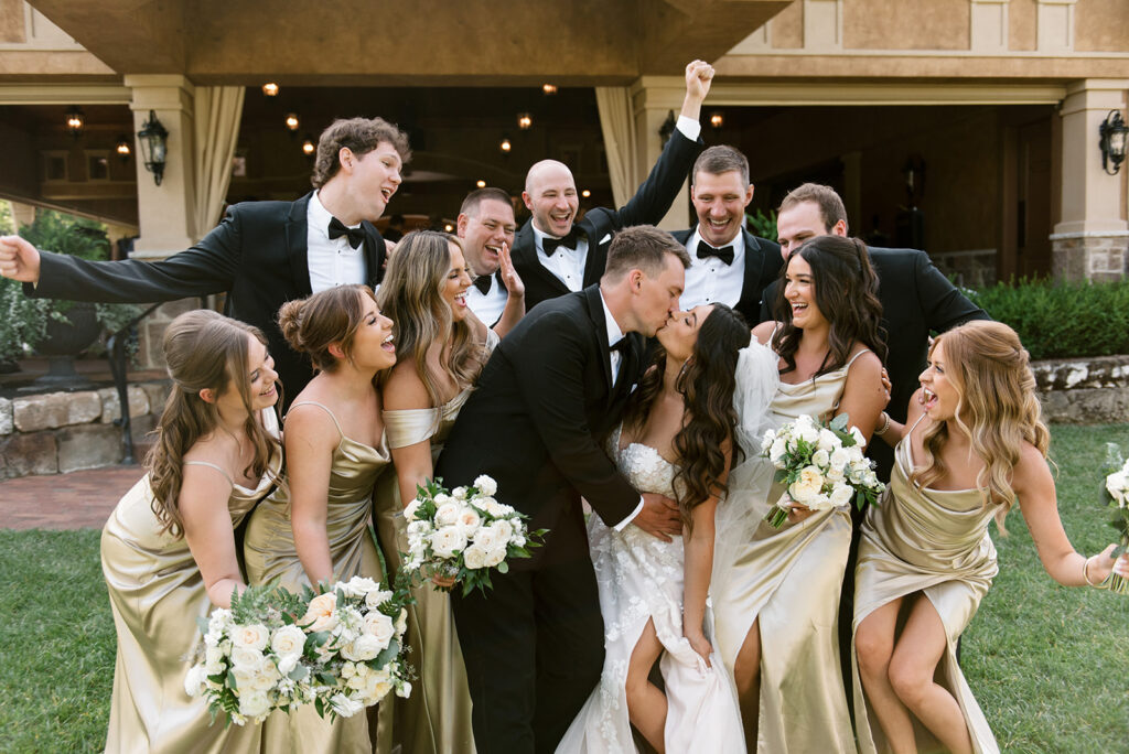 Wedding party surrounding the bride and groom as he dips her into a romantic kiss at vineyard wedding | J. Lynne Photography