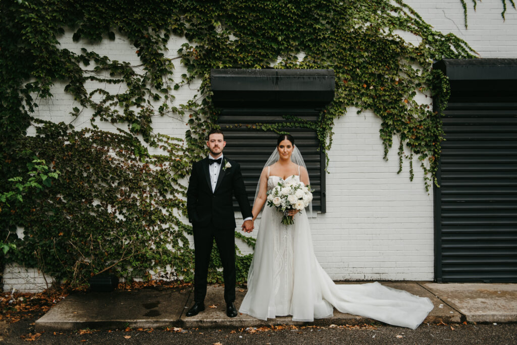 Bride and groom standing in front of a white brick wall covered in vines at the Madison Wedding Venue in Cleveland, Ohio | J. Lynne Photography