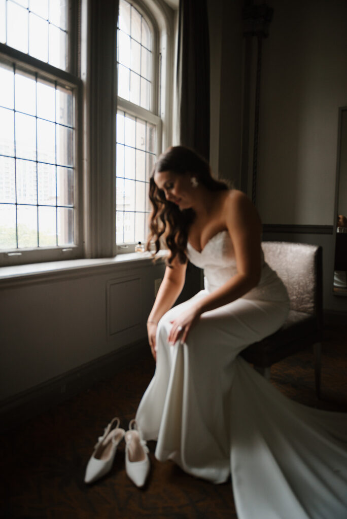 Bride putting on her wedding shoes by the window at the Tudor Arms Hotel, OH | J. Lynne Photography